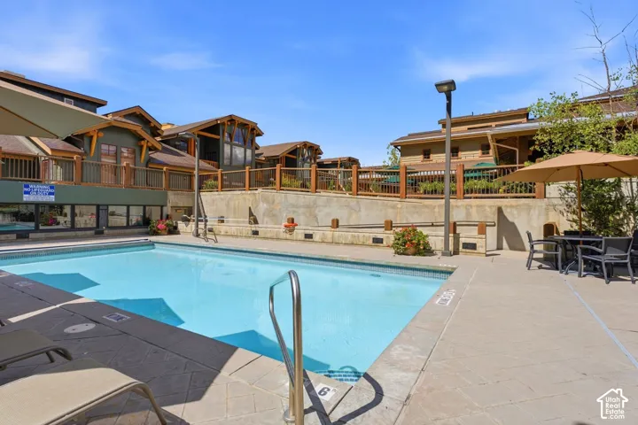 Outdoor swimming pool with integrated steps, surrounding stone-look decking, and adjacent buildings featuring balconies with wooden railings