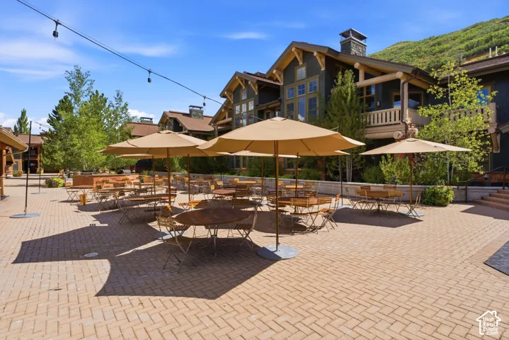 Brick paver courtyard with string lighting, surrounded by multi-story architecture with balconies, and a mountain backdrop