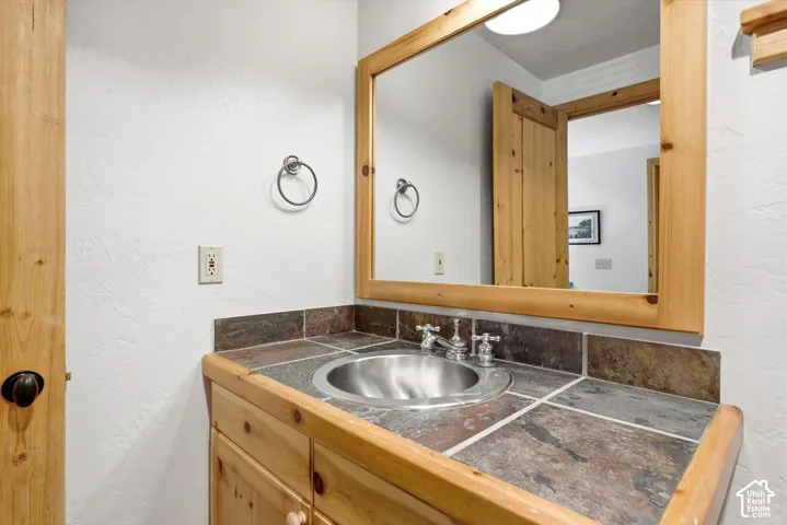 Wooden vanity with a built-in stainless steel sink, tile countertop, and a framed mirror