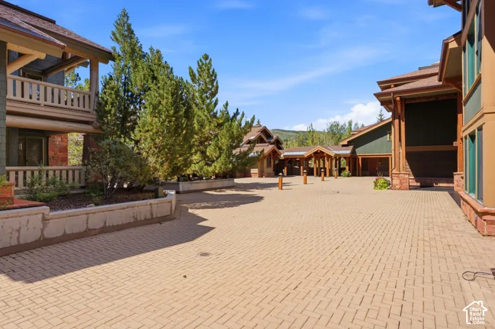 Expansive paver courtyard with architectural buildings, mature evergreen landscaping, and covered entryways