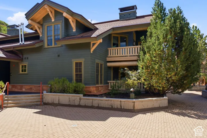 Gable roofline with exposed wood trusses, dark green siding, stone accent base, multi-pane windows, and a paved brick courtyard