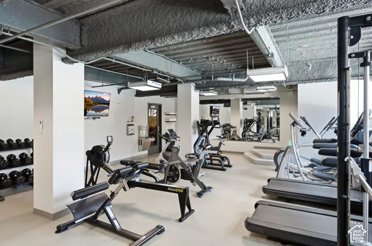 Fitness center featuring various exercise equipment, wall-mounted television, full-length mirrors, and recessed lighting
