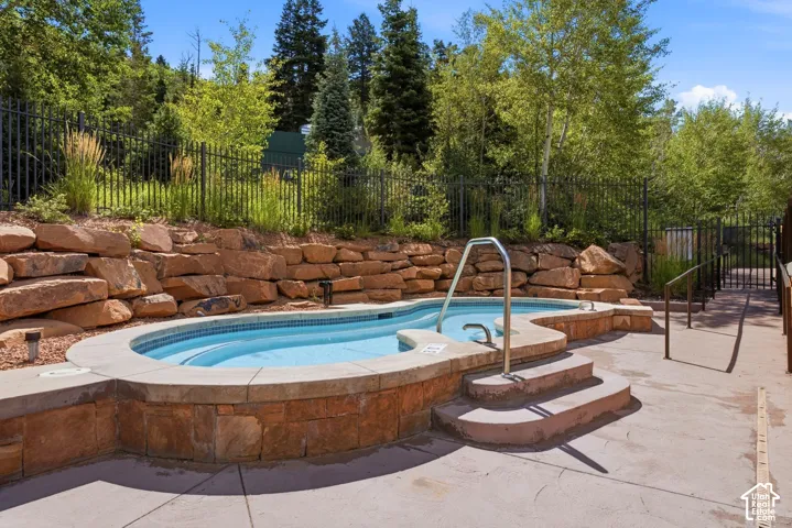 Two-tiered pool with integrated steps and handrails, complemented by a natural stone retaining wall and surrounding paved patio