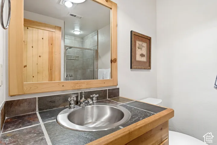 Wood-finish vanity with a drop-in stainless steel sink, tile countertop, and a wood-framed mirror