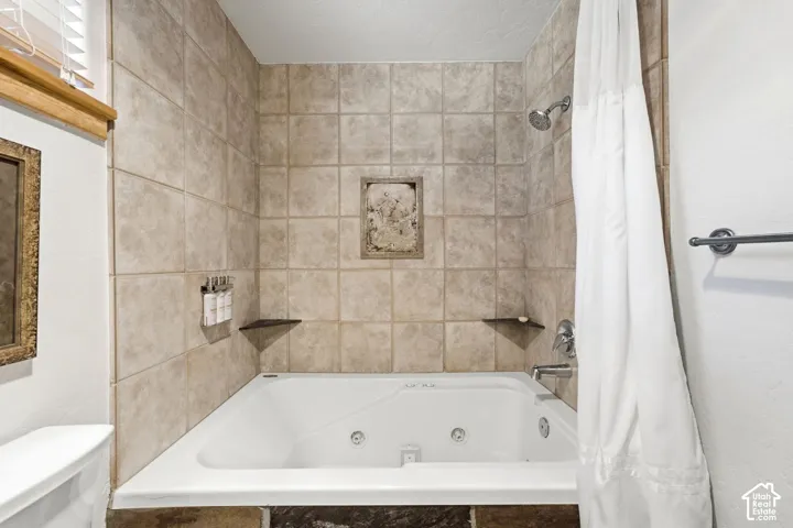 Jetted tub with tiled surround, wall-mounted showerhead, and recessed shelf