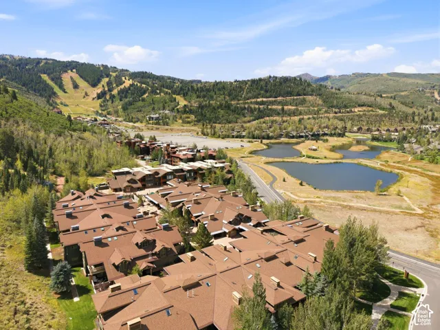 Community featuring multiple buildings with brown shingle roofs, surrounded by mature trees, and complemented by a paved road