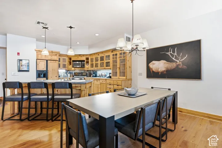Wood-finish flooring throughout, featuring a kitchen with wood cabinetry and glass-front upper cabinets, stainless steel appliances, and a peninsula with seating