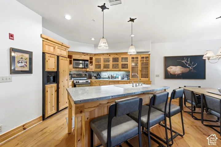 Kitchen featuring wood-finish cabinetry, stainless steel appliances, a center island with a built-in sink, and pendant lighting
