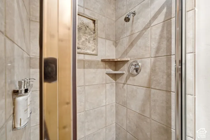 Tiled shower enclosure with built-in corner shelving, chrome fixtures, and a glass shower door