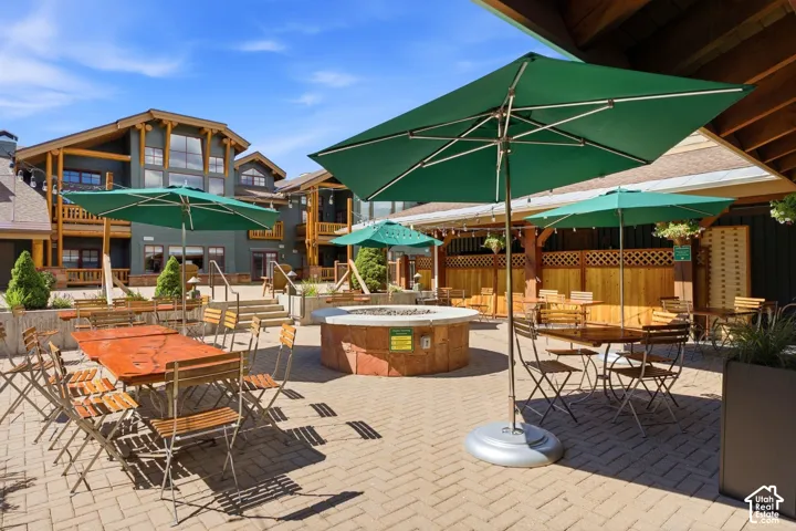 Paved patio area featuring a built-in fire pit, multiple seating areas, and architectural details including wood-beam accents and stone retaining walls