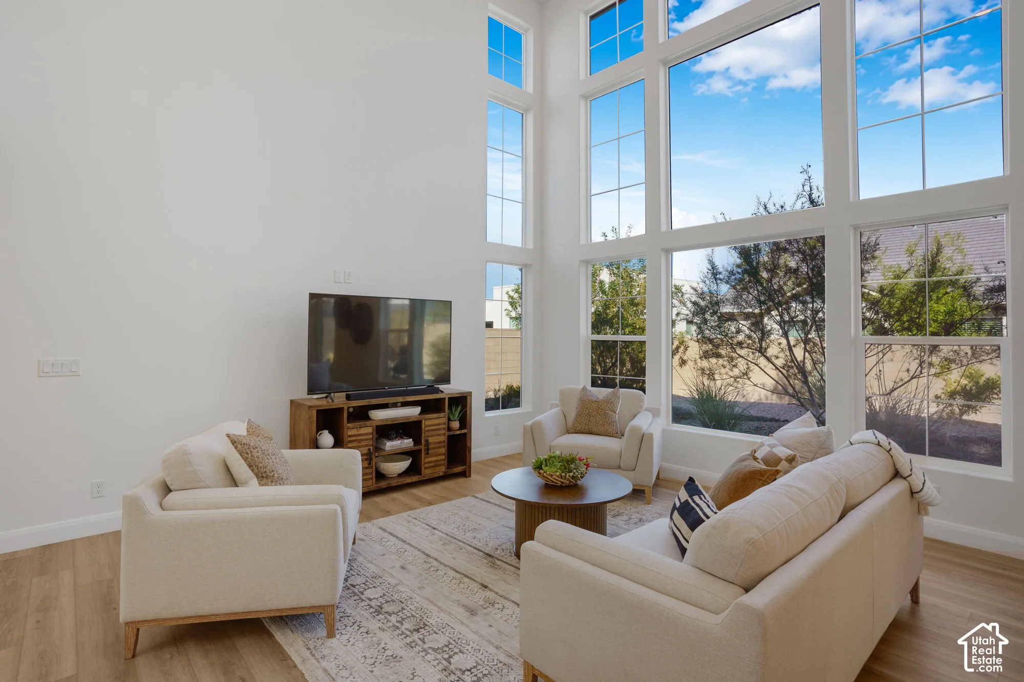 Expansive living space featuring soaring ceilings, abundant natural light, wood-finish flooring, and a media console with slatted cabinet doors