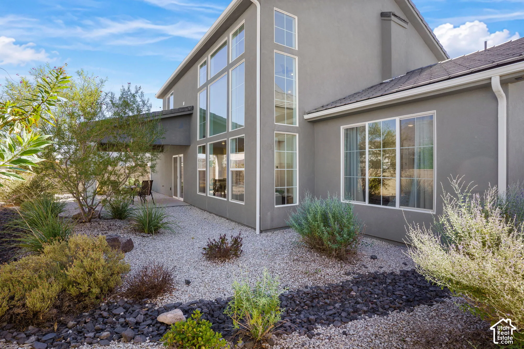Stucco exterior with multiple large windows, a covered patio, and a gravel and rock landscaped area