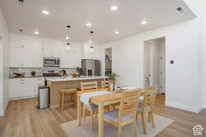 White shaker cabinetry, stainless steel appliances, wood-finish flooring, two pendant lights, and a kitchen island with seating