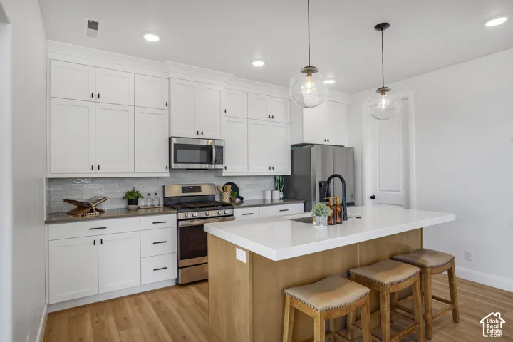 Kitchen featuring white cabinetry, stainless steel appliances, wood-finish flooring, a kitchen island with seating, and pendant lighting