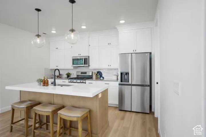 Modern kitchen featuring white cabinetry, stainless steel appliances, a center island with countertop seating, and wood-finish flooring