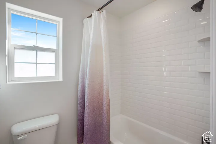 White subway tile shower surround with integrated shelving, a classic white bathtub, and a window with privacy film