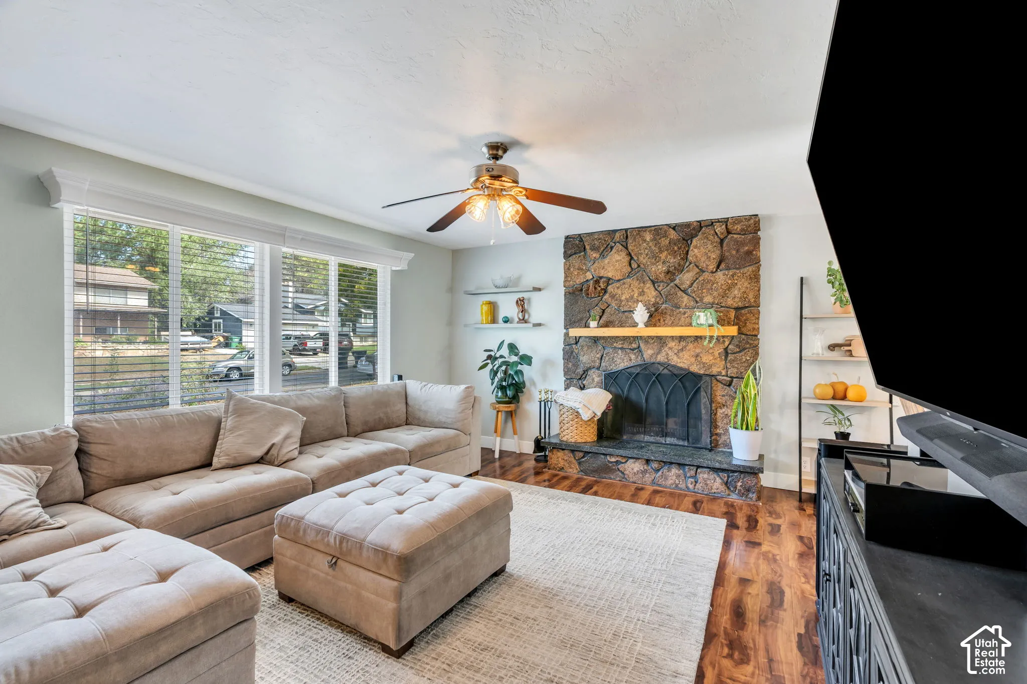 Stone-surround fireplace with a wood mantle, wood-finish flooring, and a ceiling fan