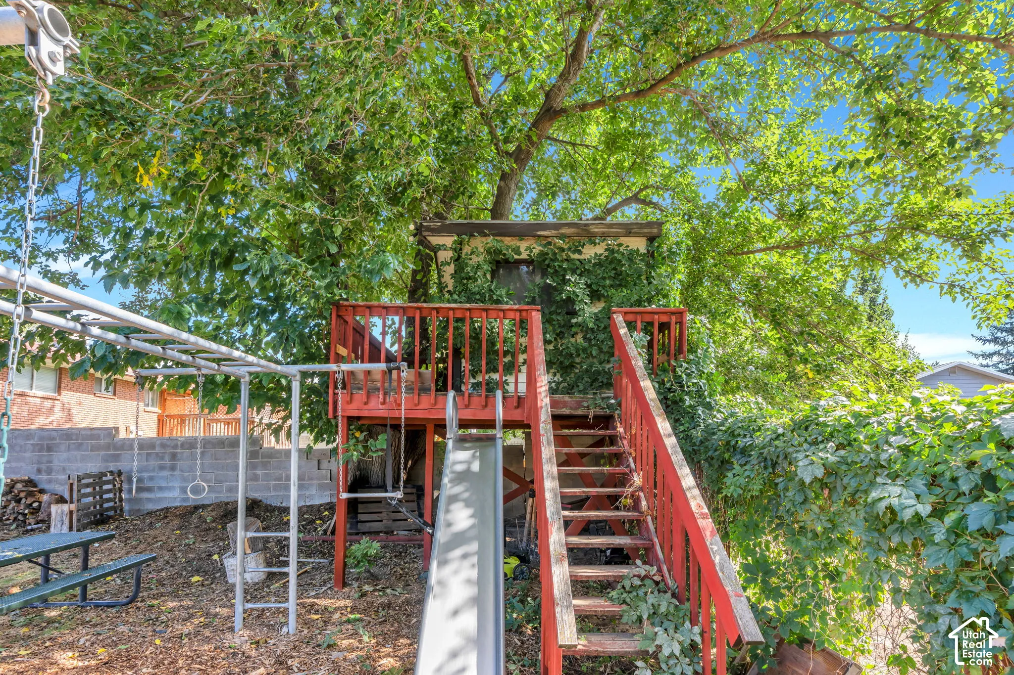 Backyard featuring a red-stained wooden play structure with stairs, an attached slide, and an overhead monkey bar set