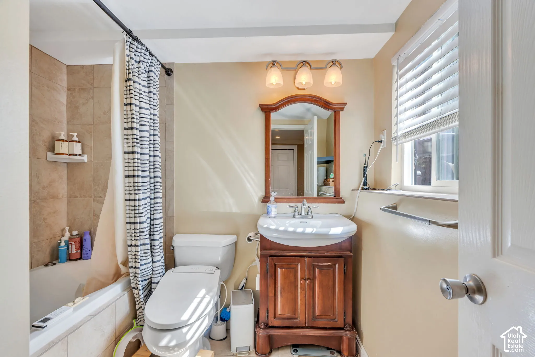 Tub and shower combination with tile surround, wood-finish vanity with an integrated sink, framed mirror, and horizontal window blinds