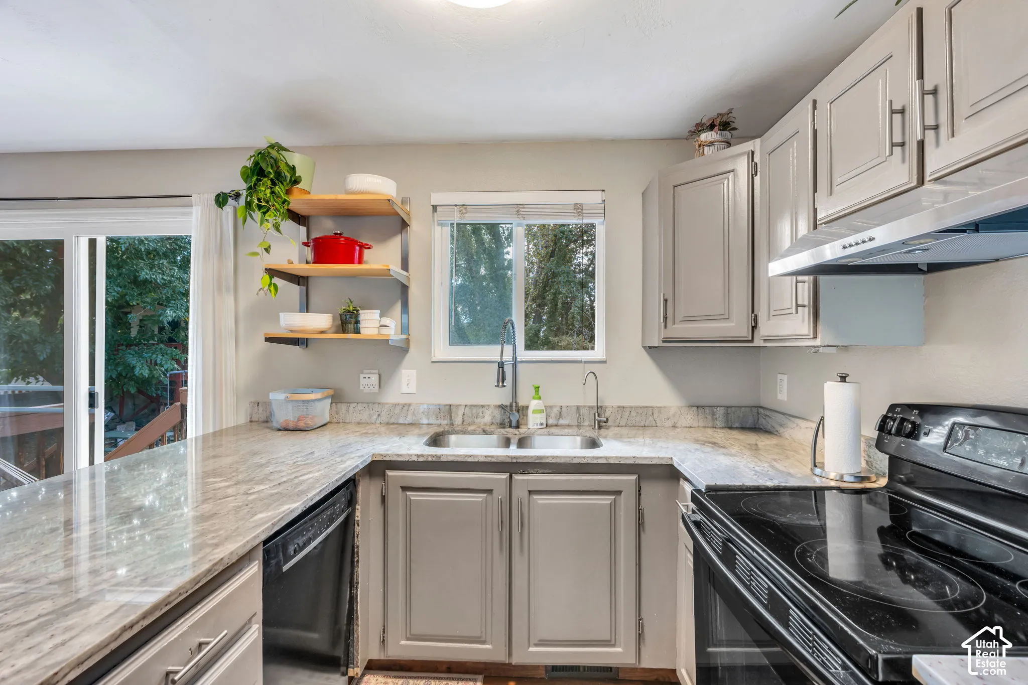 U-shaped kitchen featuring stone countertops, painted cabinetry, stainless steel sink, and built-in dishwasher