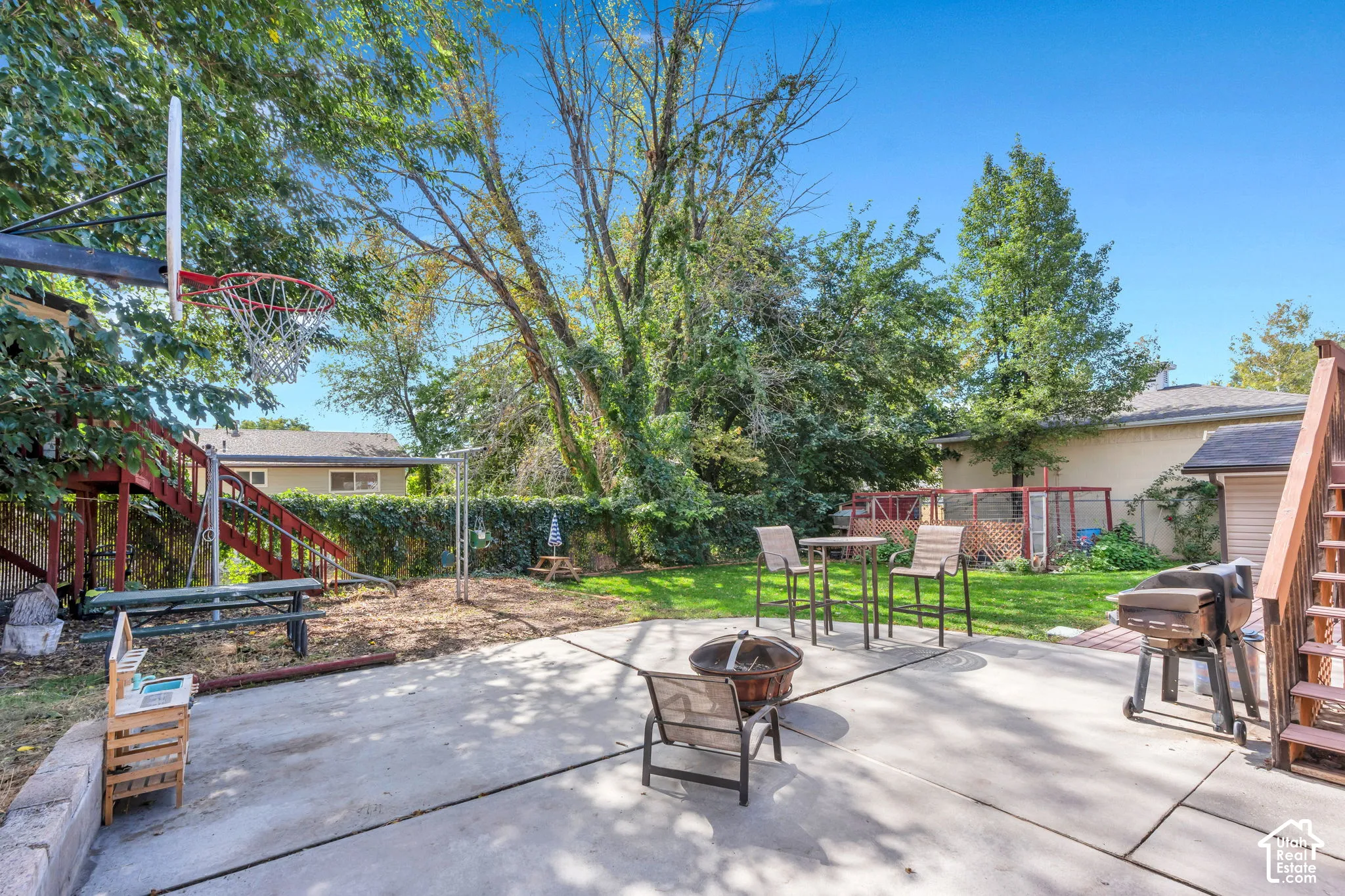 Expansive concrete patio with a fire pit, bordered by a manicured lawn and mature trees