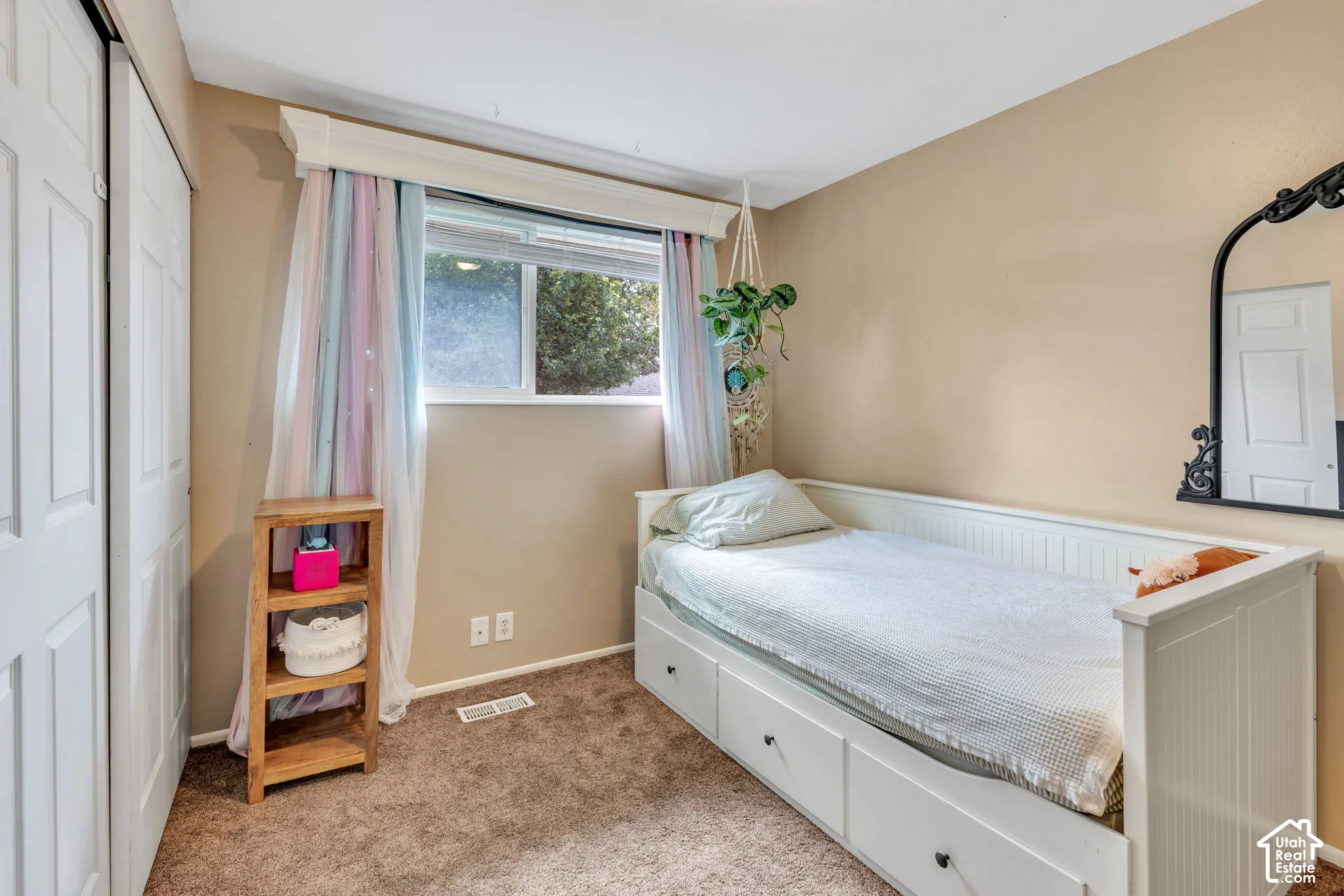 Carpeted room featuring a white paneled bed frame with integrated storage, a window with a valance, and a bi-fold closet door