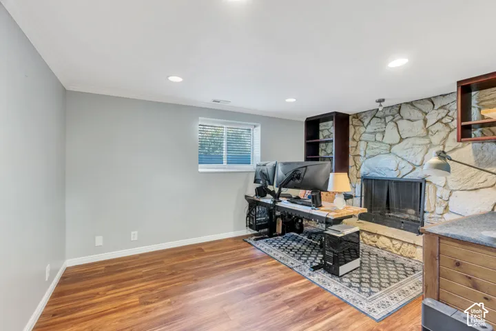 Wood-finish flooring, recessed lighting, and a stone-clad fireplace with a built-in hearth