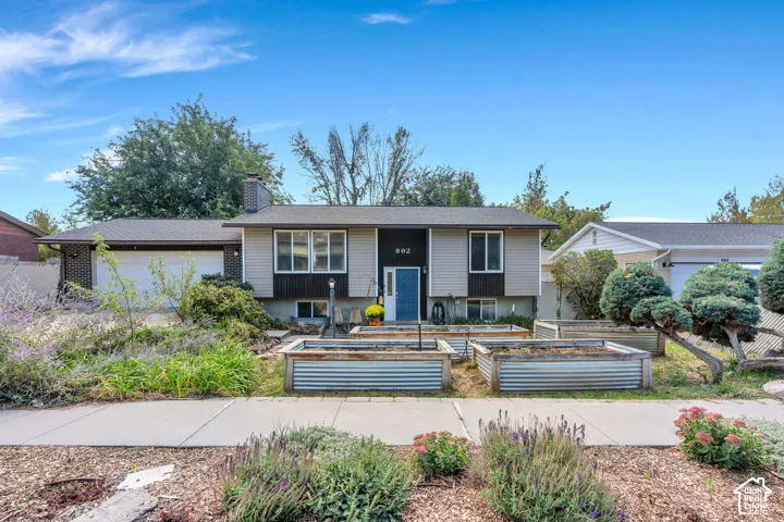 Split-level residence featuring a two-car garage, multiple raised garden beds, and a prominent chimney