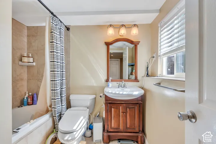 Tub and shower combination with tile surround, wood-finish vanity with an integrated sink, framed mirror, and horizontal window blinds