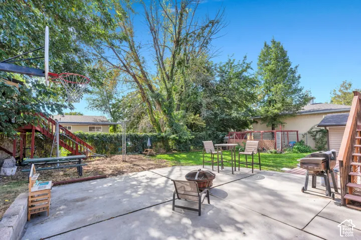 Expansive concrete patio with a fire pit, bordered by a manicured lawn and mature trees