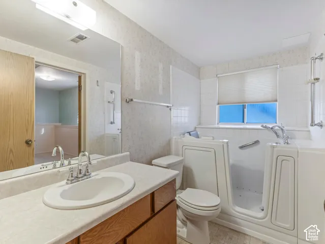 Walk-in tub with grab bars, single vanity with laminate countertop, and wall-mounted mirror