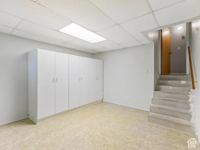 Built-in white cabinetry, textured ceiling tiles, flush-mount fluorescent lighting, light-toned flooring, and wooden handrail