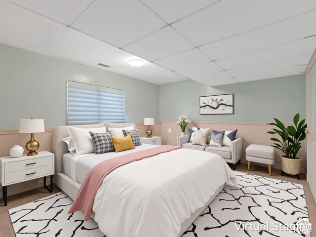 Room featuring light-toned wall paint, horizontal wainscoting, a drop ceiling, a single flush-mount ceiling light, and a window with integrated blinds