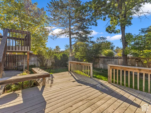 Expansive wood deck with a built-in bench, offering access to a manicured lawn and mature trees