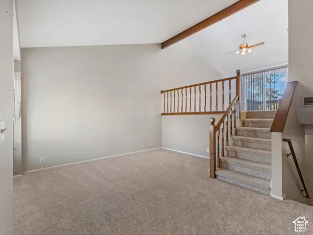 Vaulted ceiling with exposed wood beam, carpeted flooring, wood-finish staircase with baluster railing, and ceiling fan with integrated lighting