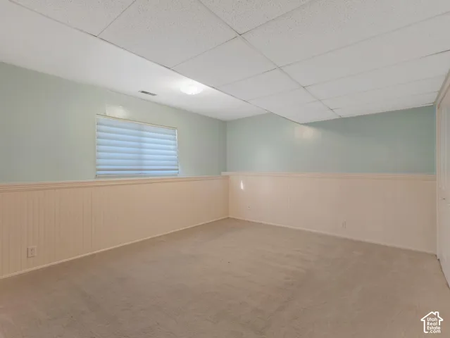 Carpeted flooring, beadboard wall paneling, drop ceiling, window with blinds, and flush-mount lighting
