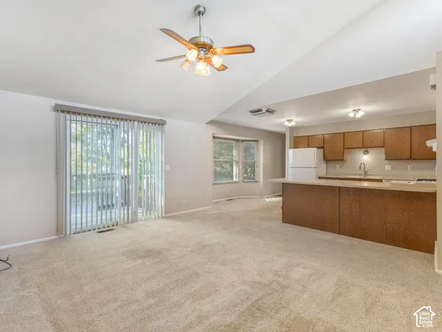Vaulted ceiling, ceiling fan with integrated lighting, glass sliding doors, wood-finish cabinetry, and a built-in kitchen island
