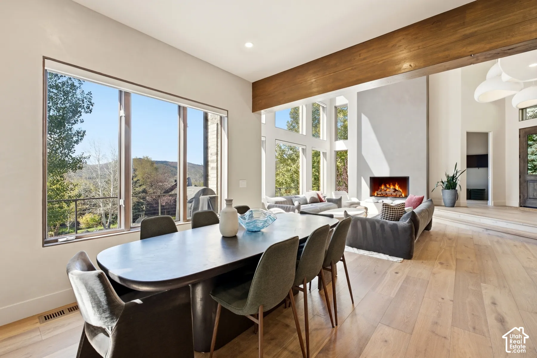 Expansive window wall, high ceilings, exposed wood beam, contemporary fireplace, and light wood-finish flooring