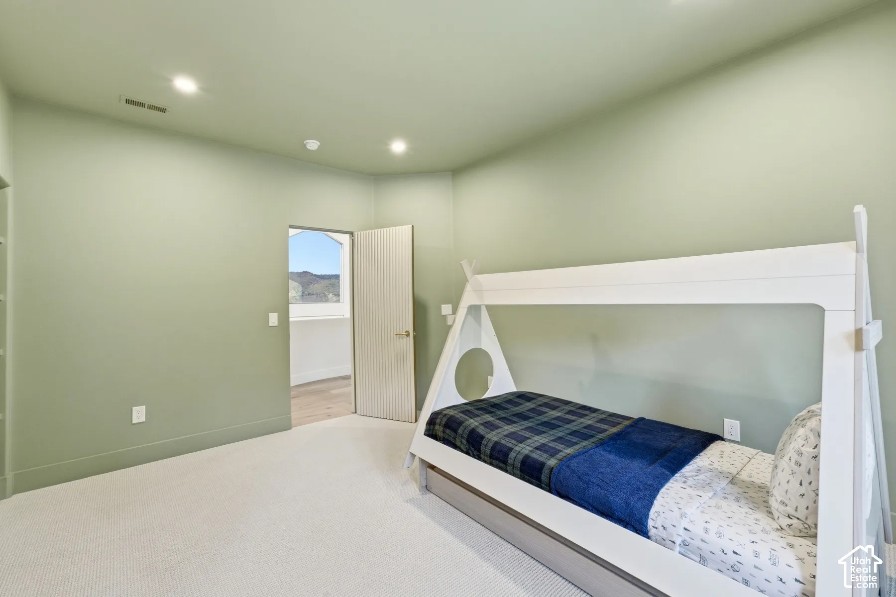 Recessed ceiling lighting, light green painted walls, light-toned carpeting, and a white interior door with horizontal paneling