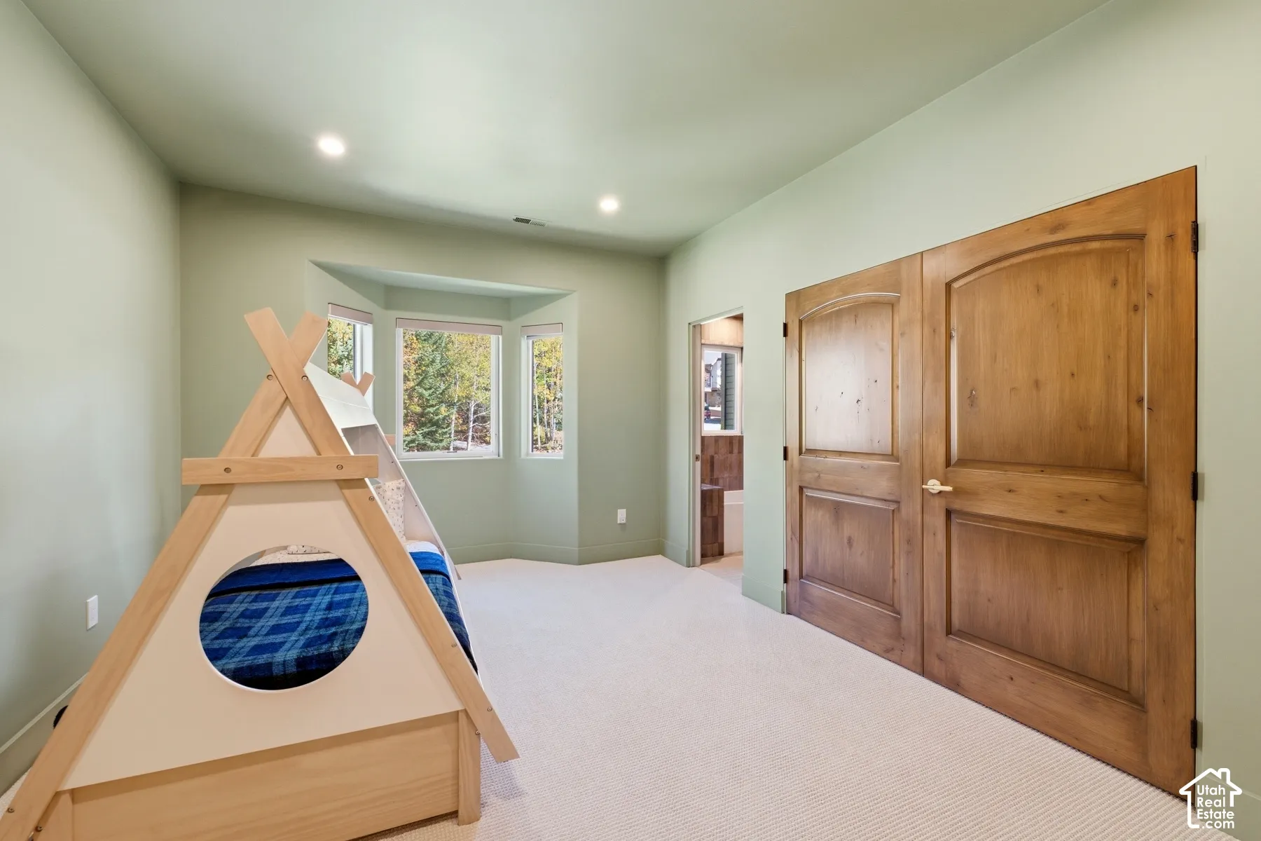 Recessed lighting illuminating the room, bay window with multiple panes, light-toned carpeting, and wood-finish doors with arched paneling