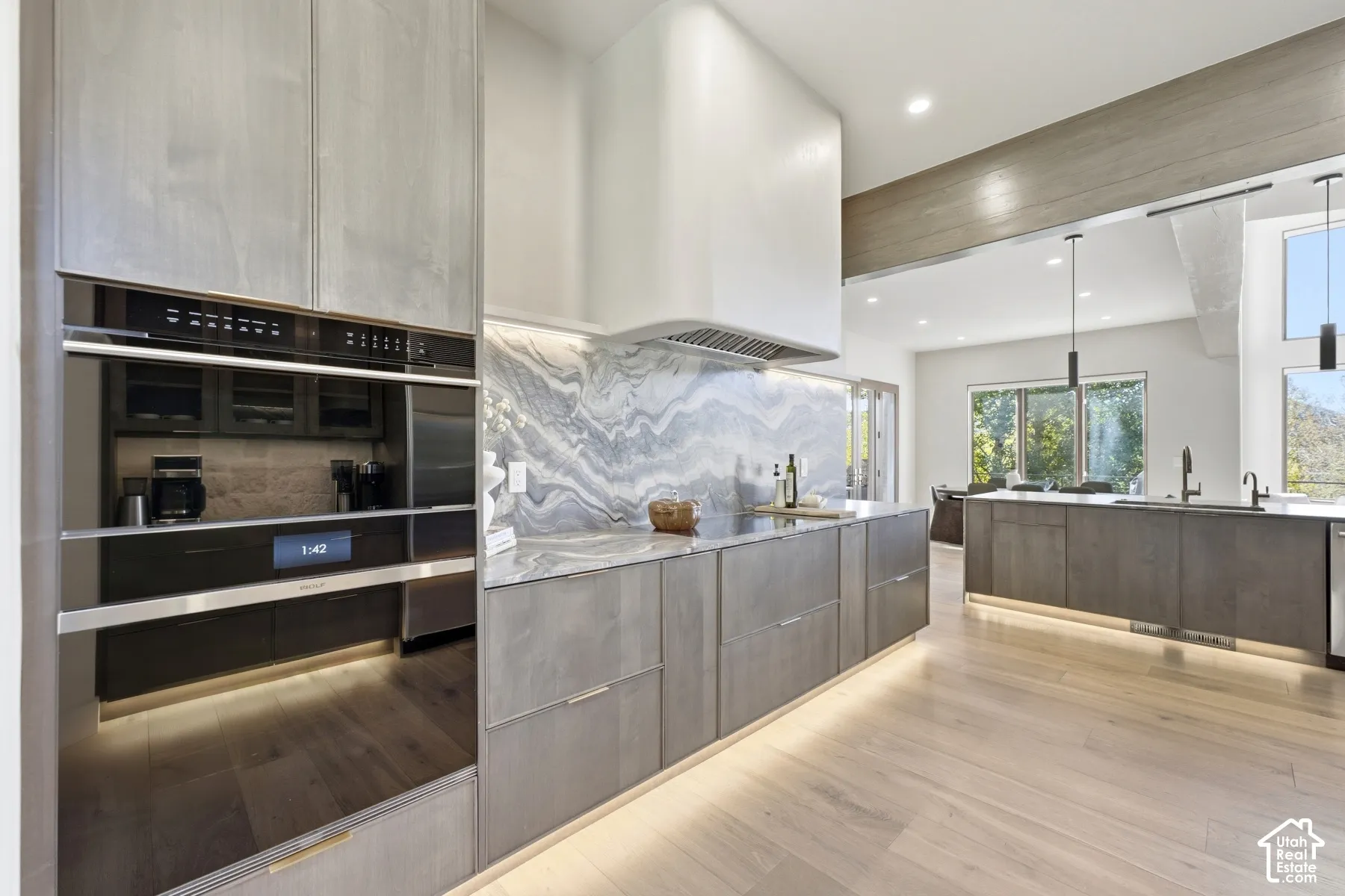 Modern kitchen featuring a waterfall-edge island with gray cabinetry, professional-grade stainless steel appliances including dual wall ovens, white quartz countertops, and a marble-pattern backsplash