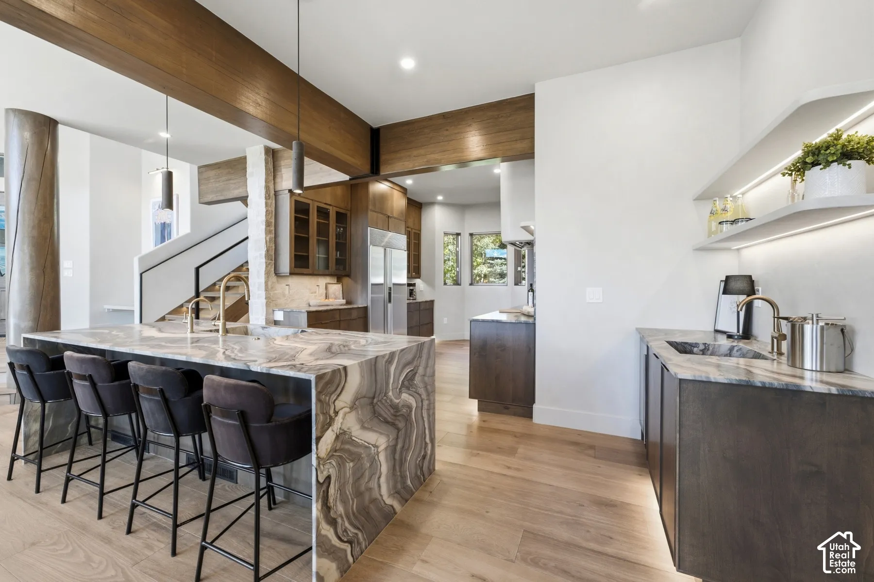 Spacious kitchen featuring a large waterfall island with integrated seating, light wood-finish flooring, and a separate wet bar with illuminated shelving