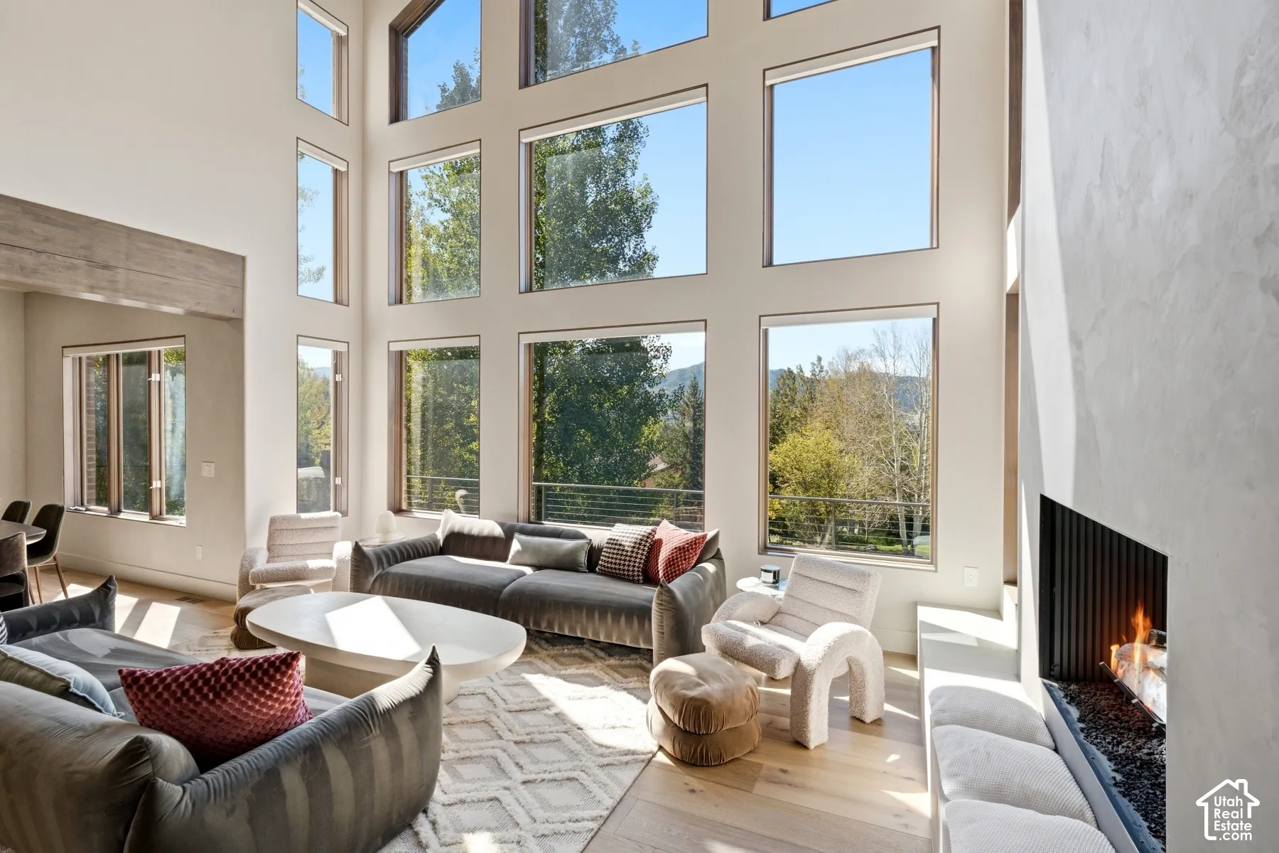 Double-height ceilings with expansive windows, light wood-finish flooring, a built-in linear fireplace, and a light-colored accent wall