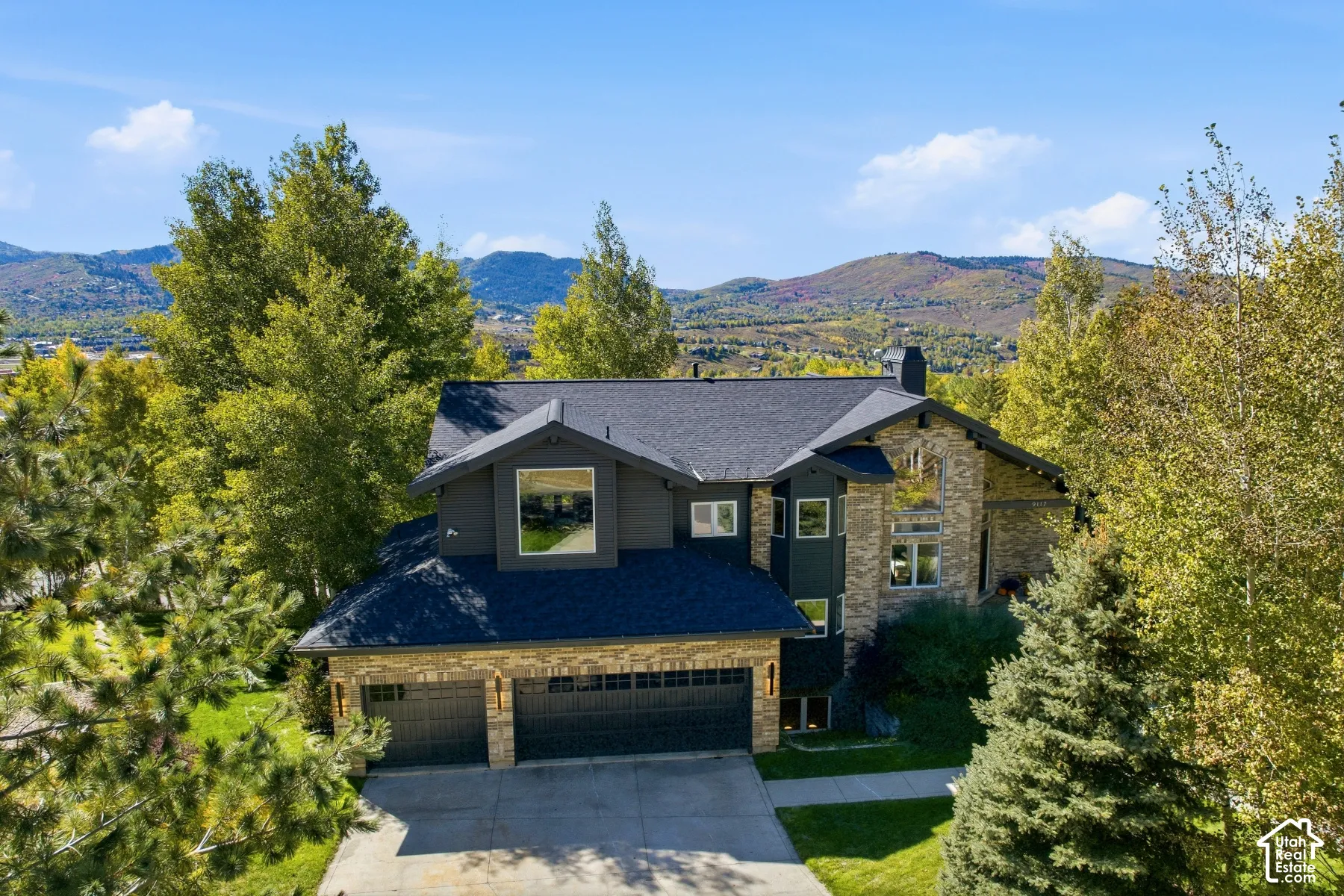 Multi-level residence featuring a dark gray roof, stone and dark siding exterior, two-car garage, and mature landscaping