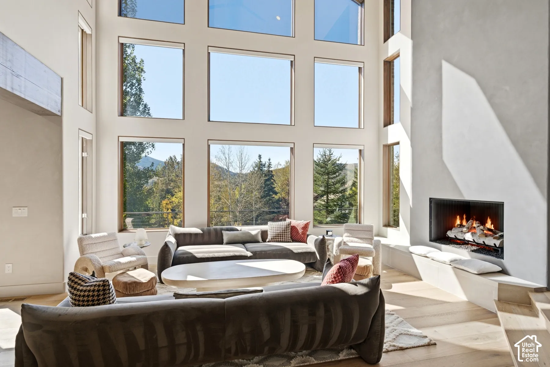 Two-story window wall, integrated fireplace with hearth seating, light wood-finish flooring, and high ceilings