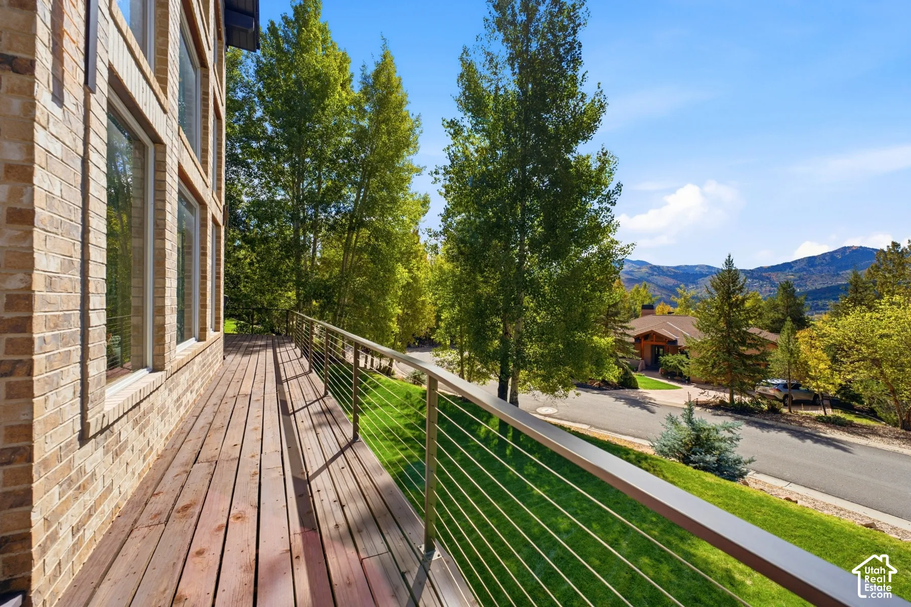 Expansive wood deck with a stainless steel cable railing system, overlooking a manicured lawn and distant mountains