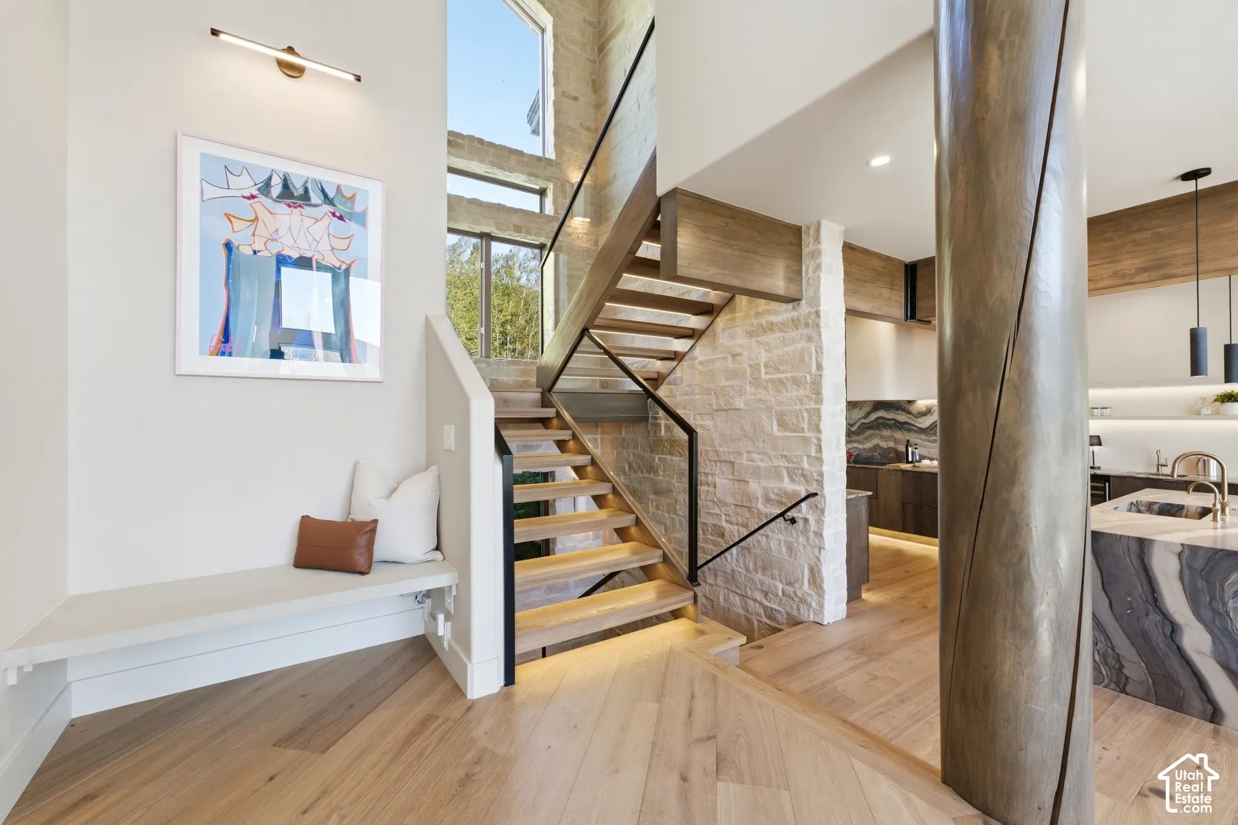 Hardwood flooring, natural stone wall, open-tread staircase with glass railing, built-in bench, and high ceilings