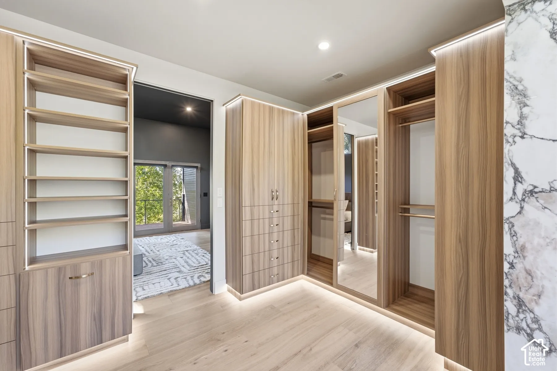 Custom closet system featuring wood-finish cabinetry, integrated lighting, built-in shelving, and mirrored doors