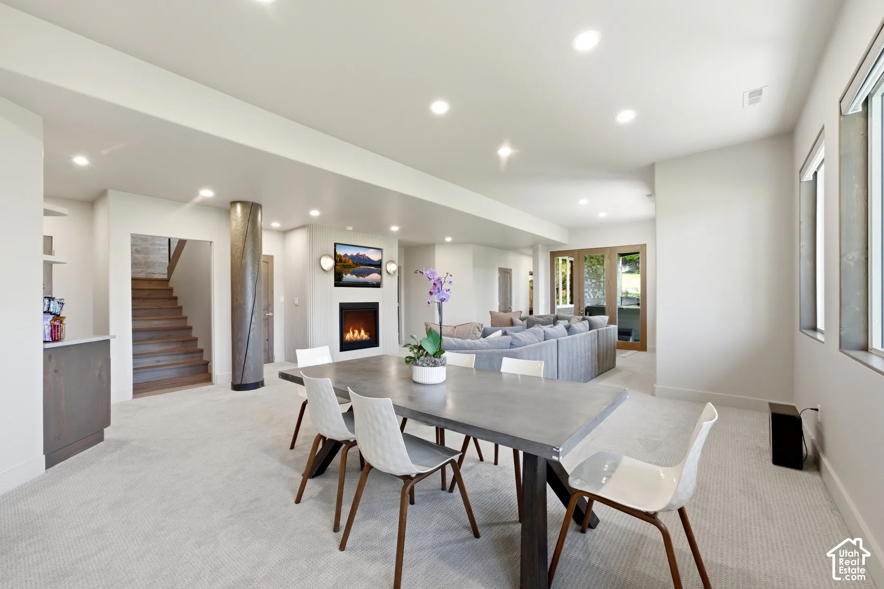 Recessed lighting illuminates an open-concept room featuring a built-in fireplace, a built-in wet bar, and a wooden staircase
