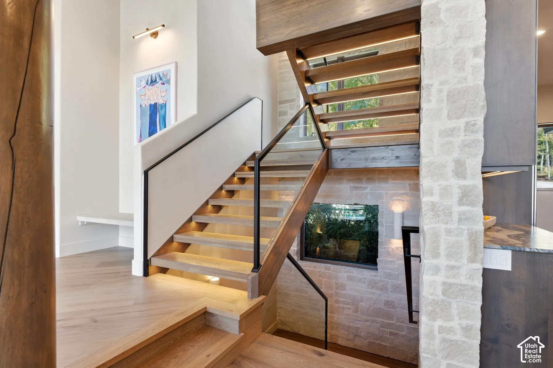 Floating wood staircase with integrated tread lighting, glass panel railing, natural stone wall accents, and wood-finish flooring